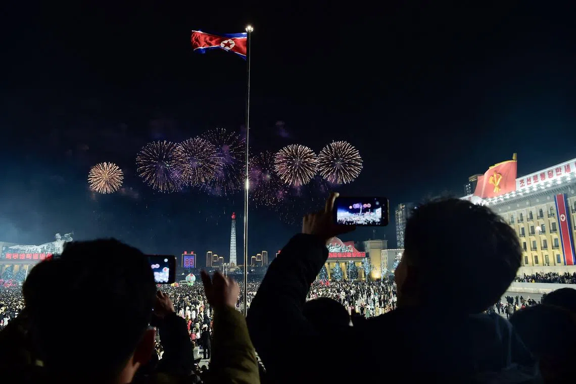 New Year fireworks burst behind North Korea's national flag at Kim Il Sung Square in Pyongyang on January 1, 2025. (Photo by KIM Won Jin / AFP)