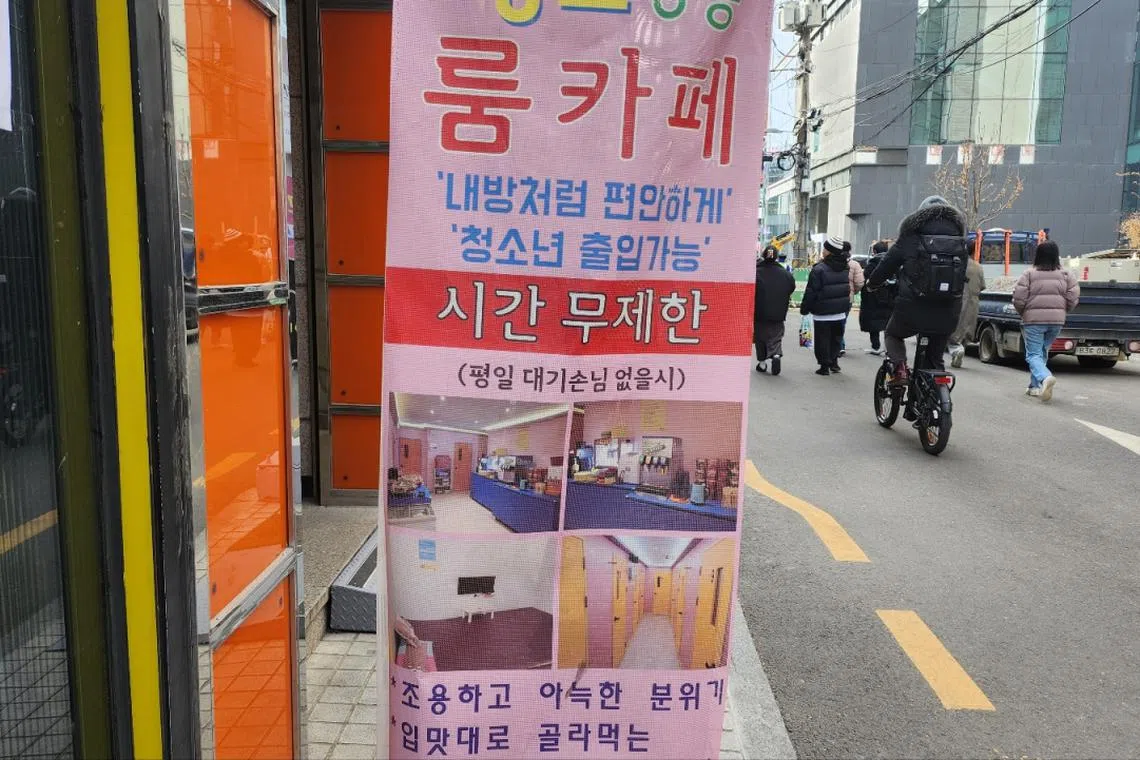 Pedestrians walking by a banner advertising a room cafe in Mapo-gu, Seoul, which mentions "Adolescents are allowed". 