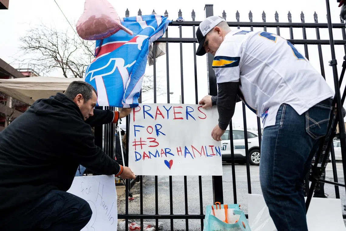 Football fans tape a sign to a fence during a vigil outside the University of Cincinnati Medical Centre where Buffalo Bills safety Damar Hamlin lies in intensive care after suffering a cardiac arrest during the NFL game against the Cincinnati Bengals.