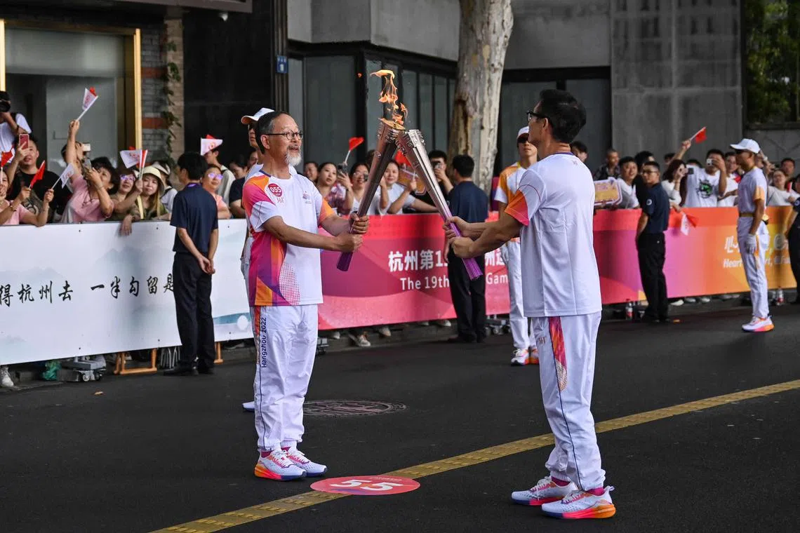 Archaeologist Xu Tianjing (left) and writer Mai Jia exchange the flame during the Asian Games torch relay in Hangzhou.
