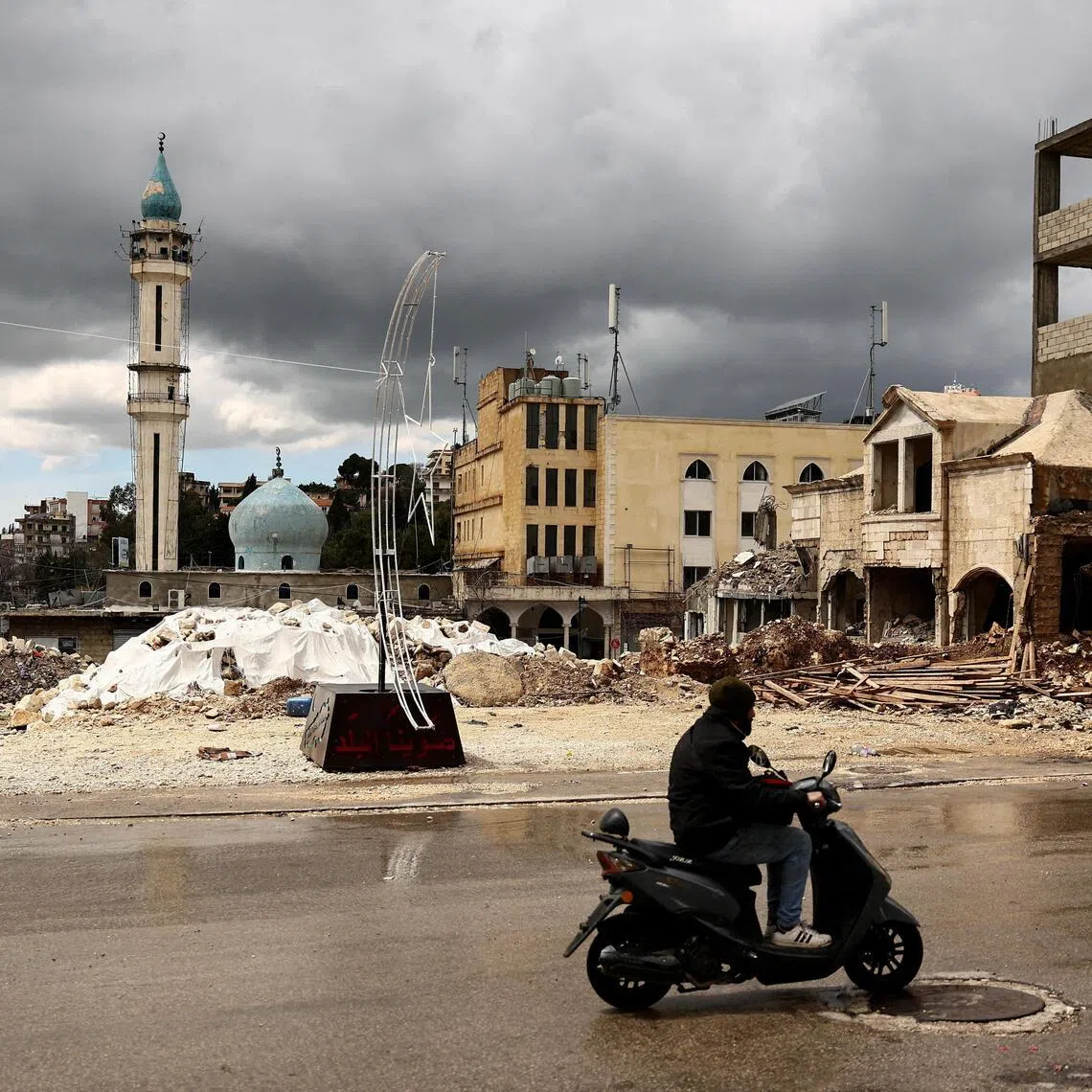 A man rides a motorcycle past the rubble of a site damaged in an Israeli strike in Nabatieh, Lebanon.