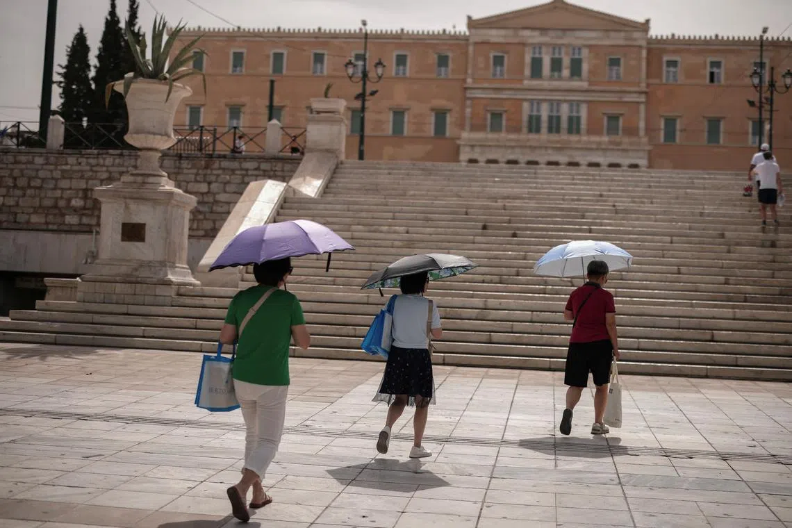 Tourists holding umbrellas walk on Syntagma Square as a heatwave hits Athens, Greece, on June 13, 2024.