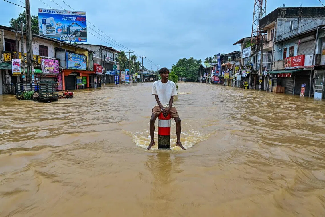 A man sits on a divider in the middle of a flooded road after heavy rainfall in Kaduwela on the outskirts of Colombo on Nov 29, 2025.