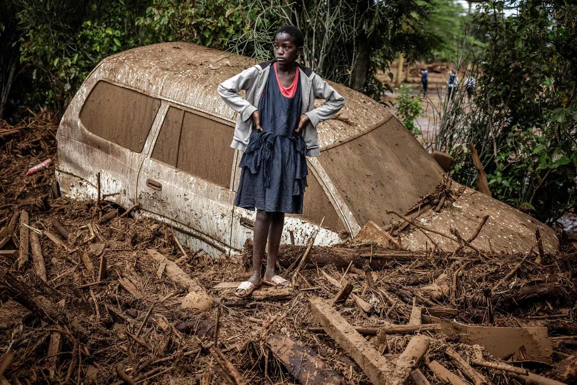 A girl looks on next to a damaged car buried in mud in an area heavily affected by torrential rains and flash floods in the village of Kamuchiri, near Mai Mahiu, on April 29, 2024. At least 45 people died when a dam burst its banks near a town in Kenya's Rift Valley.