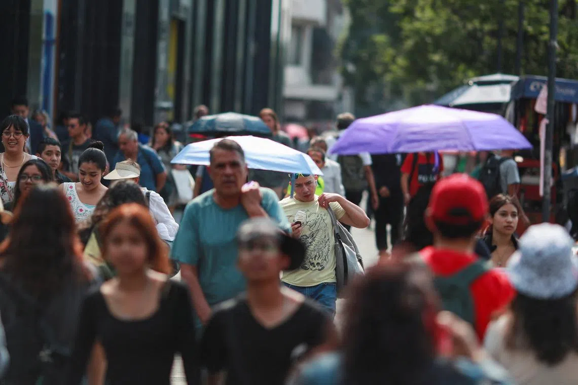 People cover themselves with umbrellas next to others as they walk along a sidewalk during high temperatures, in Mexico City, Mexico May 9, 2024. REUTERS/Henry Romero