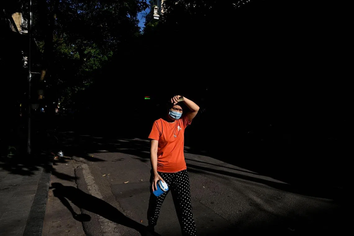 (FILES) In this file illustration photo taken on June 18, 2021, a woman wearing a face mask shields her face from the sun while walking along a street in the old quarters of Hanoi. - Vietnam posted a record high temperature of 44.1 degrees Celsius on May 6, 2023, officials said. (Photo by Manan VATSYAYANA / AFP)