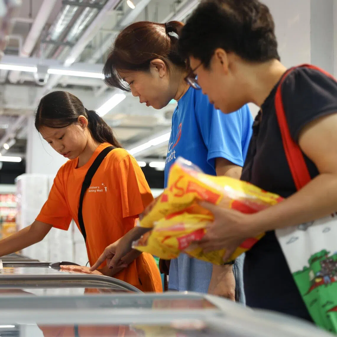 (From left) Najwa Chua Ai Xin, 12, UOB Heartbeat volunteer Ho Ying Ying and ST reporter Chor Khieng Yuit searching for frozen food on Najwa’s grocery list during a July 22 shopping run.