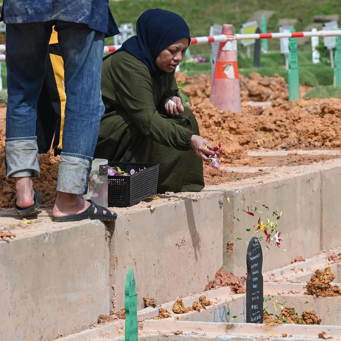 Madam Siti, the mother of the 13-year-old boy who died after falling into the Kallang River, sprinkling flowers over his grave on Feb 27.