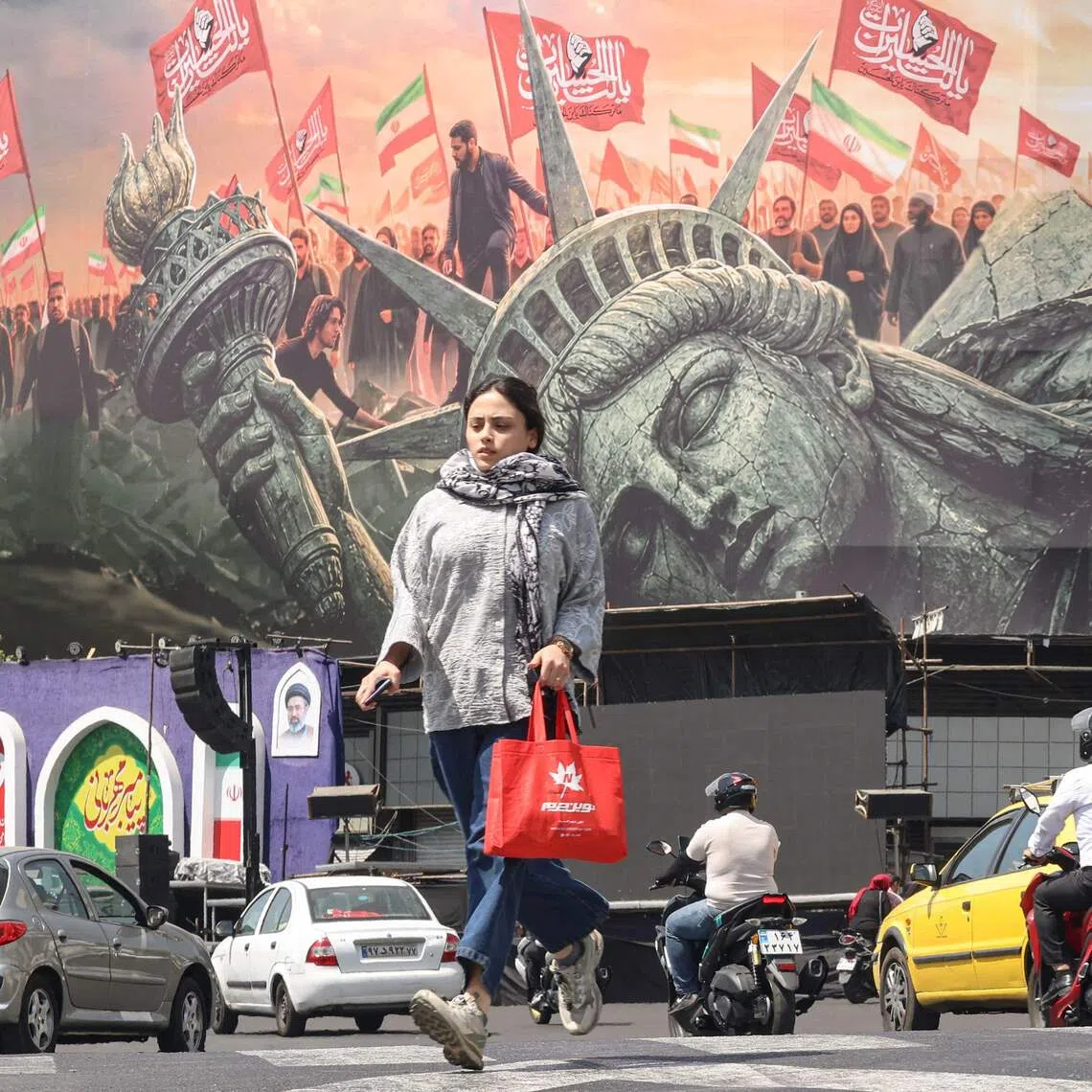 A woman crosses as motorists drive past an anti-US billboard at Enghelab Square in Tehran. Iran, a major oil producer with some of the world’s cheapest fuel, has for years heavily subsidised petrol.