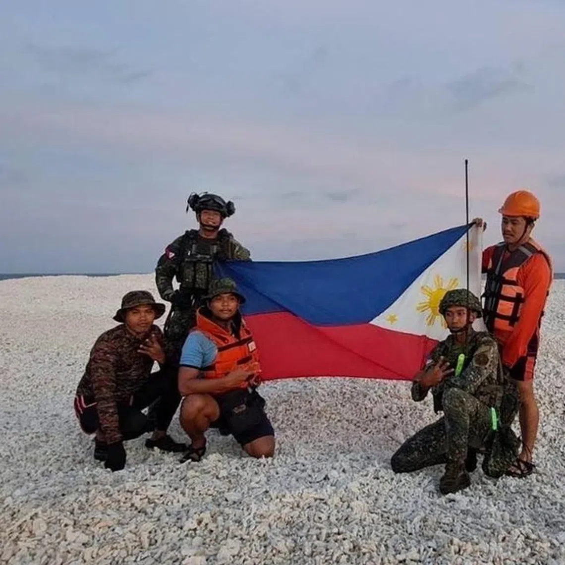 Philippine coast guard personnel holding a Philippine flag during an inter-agency maritime operation on Sandy Cay.