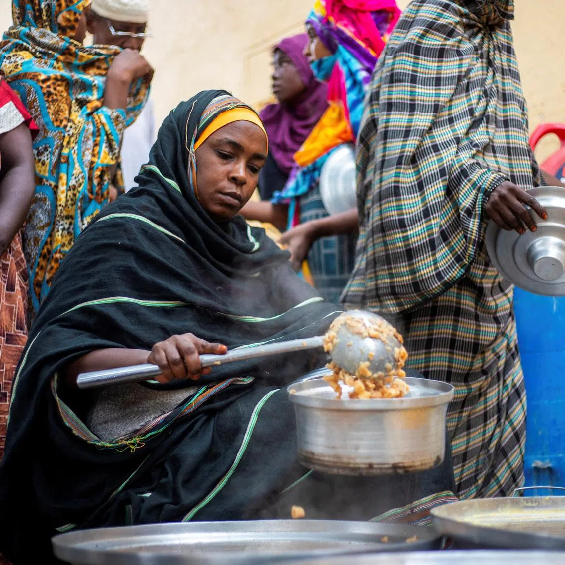 FILE PHOTO: A Sudanese woman from a community kitchen run by local volunteers distributes meals for people who are affected by conflict and extreme hunger and are out of reach of international aid efforts, in Omdurman, Sudan, August 22, 2024. REUTERS/Mazin Alrasheed/File Photo