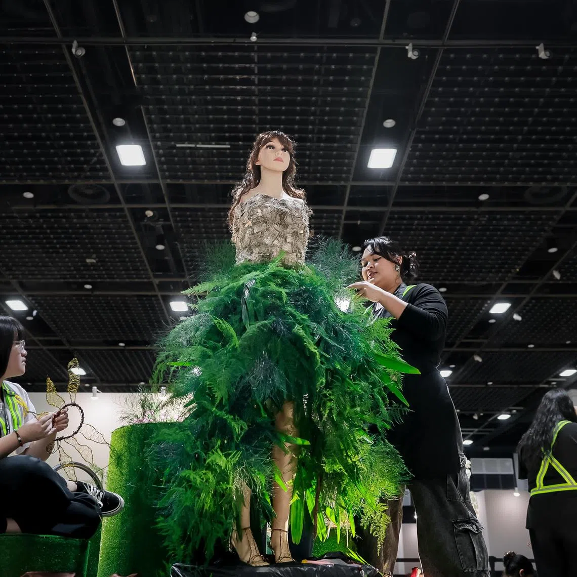 ITE College Central Year 2 Nitec in Floristry student Chua Zhi En Sera (right) with her team's Bark Forest Fairy dress on a mannequin on Aug 1, 2024, for the Wearable Floral Art Showcase by the Singapore Garden Festival held at Suntec Singapore Convention & Exhibition Centre.