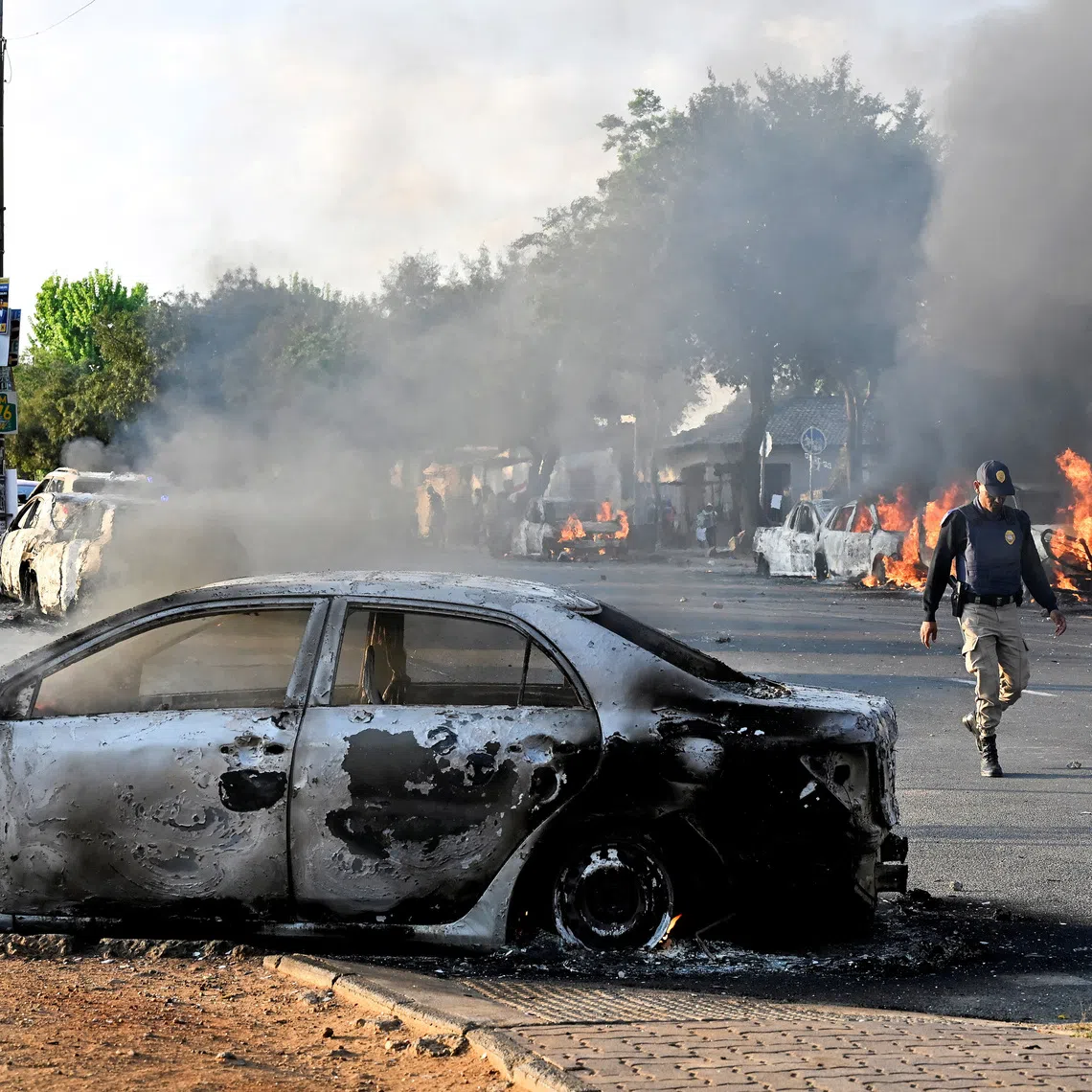 A police officer walks past burning vehicles during unrest following anti-migrant protests, where residents clashed with foreign-owned shopkeepers, and vehicles were set alight, after months of anti-migrant demonstrations that have drawn international criticism, in Soweto, South Africa, October 8, 2026. REUTERS/Stringer