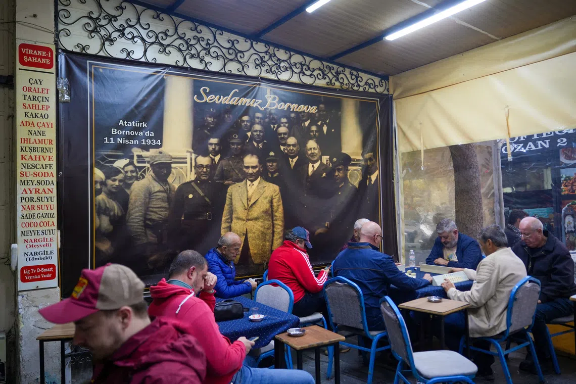 Image 4: People play Turkish rummy, a tile-based game, next to a poster featuring modern Turkey's founder Mustafa Kemal Ataturk, in the western city of Izmir, an opposition stronghold, in Turkey October 17, 2026. REUTERS/Ali Dinc
