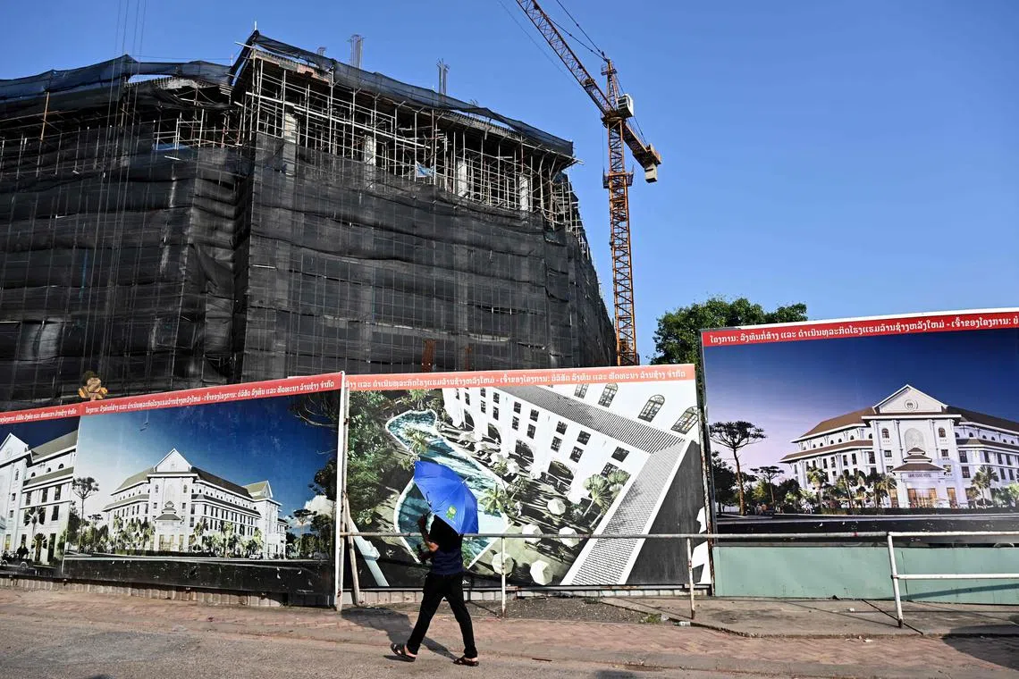 This photo taken on October 8, 2024 shows a man walking past an under-construction hotel in Laos' capital Vientiane. Suffocating under a mountain of debt to China, communist Laos is struggling to tame rampant inflation, with food prices rising so sharply that a growing number of households are resorting to foraging. (Photo by TANG CHHIN Sothy / AFP) / To go with 'LAOS-ECONOMY-INFLATION-DEBT,FOCUS' by Thanaporn Promyamyai and Damon Wake