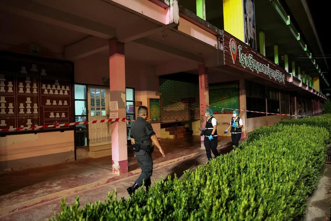 Members of the forensic team and a police officer walk near the building inside Patongprathankiriwat School.