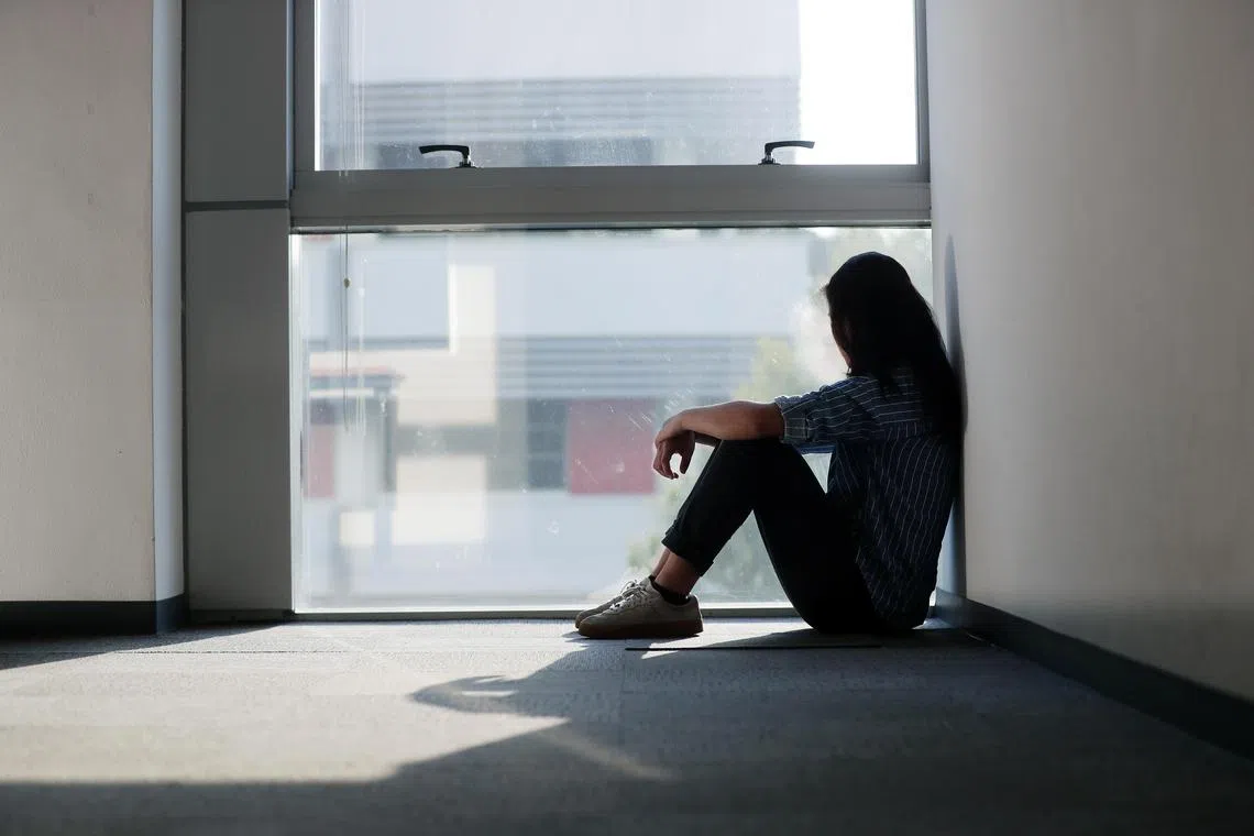 Posed photo of a girl who is stressed and depressed, seating on a floor behind a glass window.