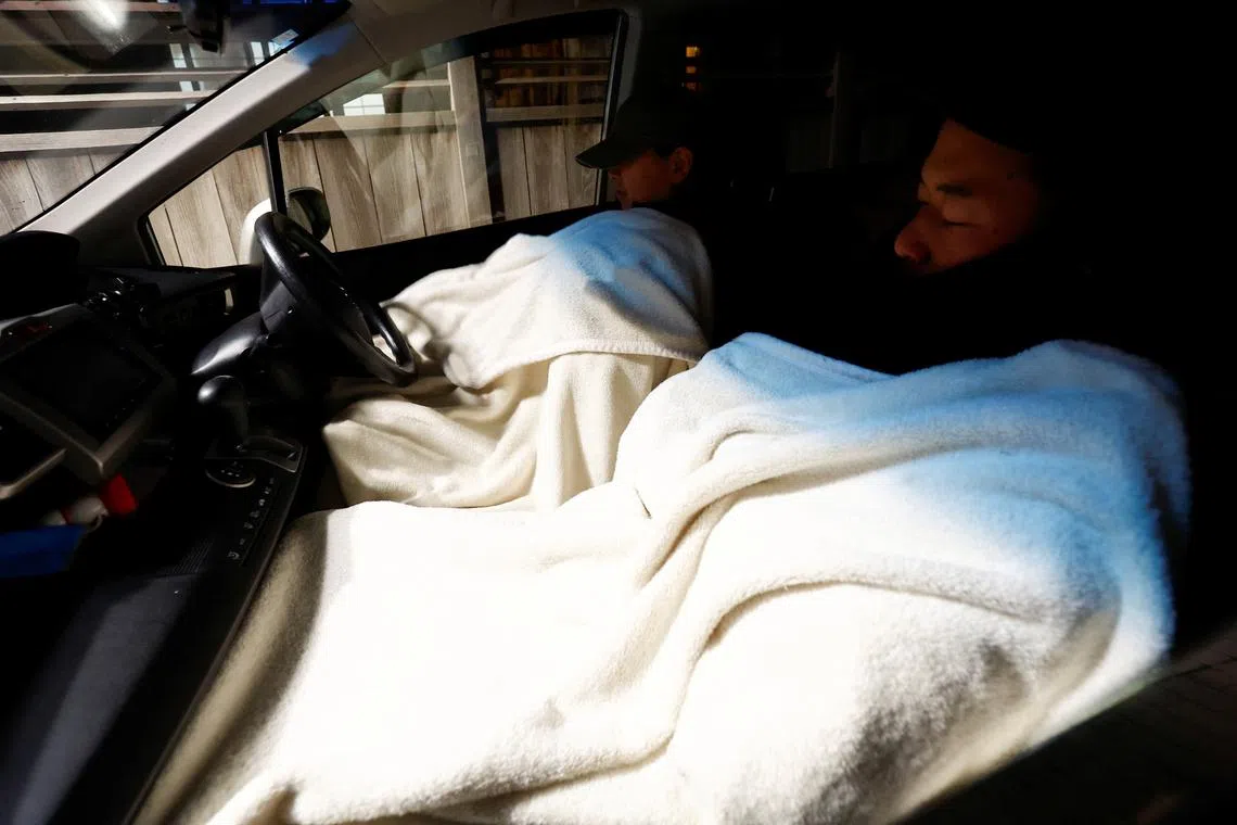 Shinto shrine priest Ayuko Noto and her cousin Fumito Yamada sleeping in their car, as they fear further devastation resulting from aftershocks following the earthquake, near their Juzo Shinto shrine in Wajima , Ishikawa Prefecture, Japan, Jan 5, 2024. 