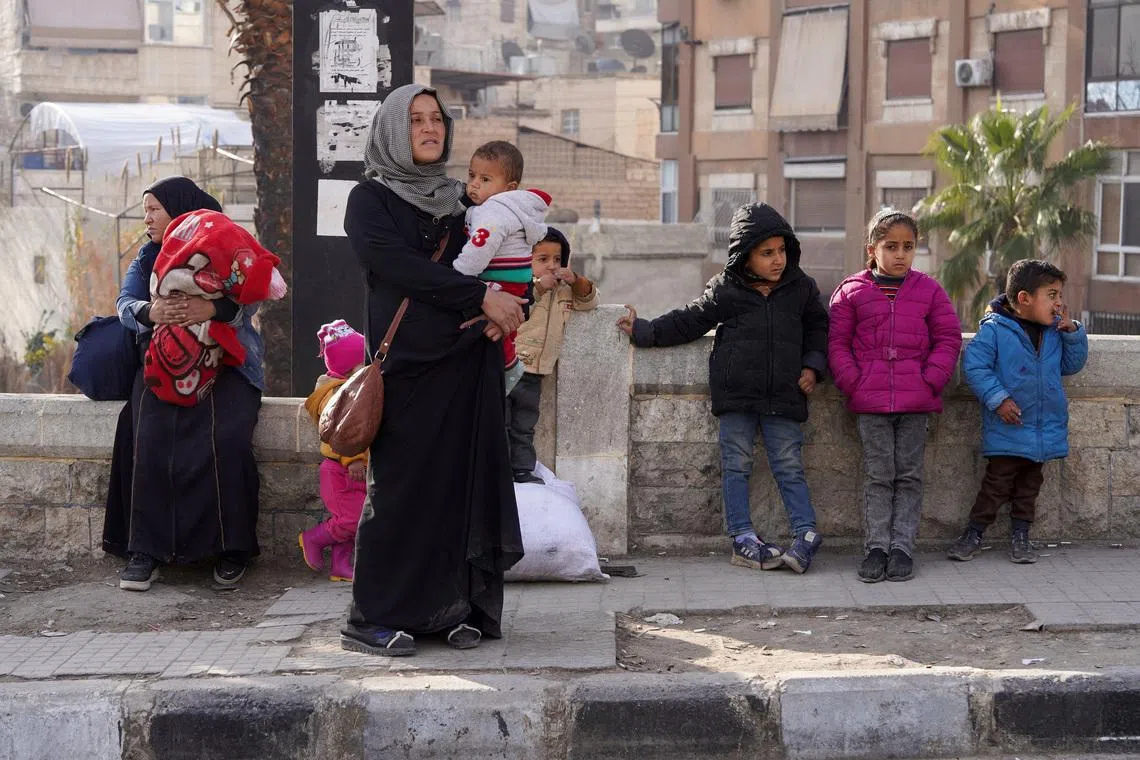 A woman carries her child as she flees, following renewed clashes between the Syrian army and the Syrian Democratic Forces (SDF), in Aleppo, Syria, January 7, 2026. REUTERS/Karam al-Masri