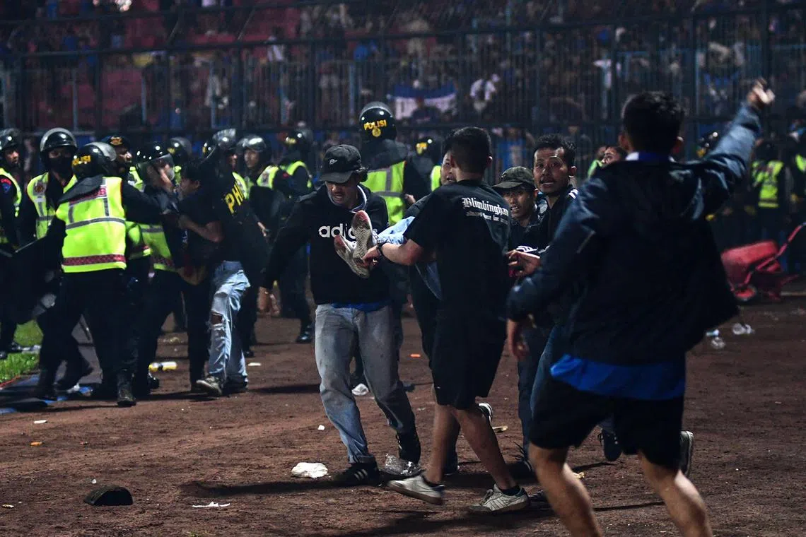 (FILES) In this picture taken on October 1, 2022, a group of people carry a man after a football match between Arema FC and Persebaya Surabaya at Kanjuruhan stadium in Malang, East Java. The Indonesian stadium where 135 people died in October 2022 in one of football's worst tragedies lies empty but intact, despite government pledges to demolish it and rebuild a safer site. (Photo by AFP) / TO GO WITH fbl-Indonesia-stampede, FOCUS by Jack MOORE