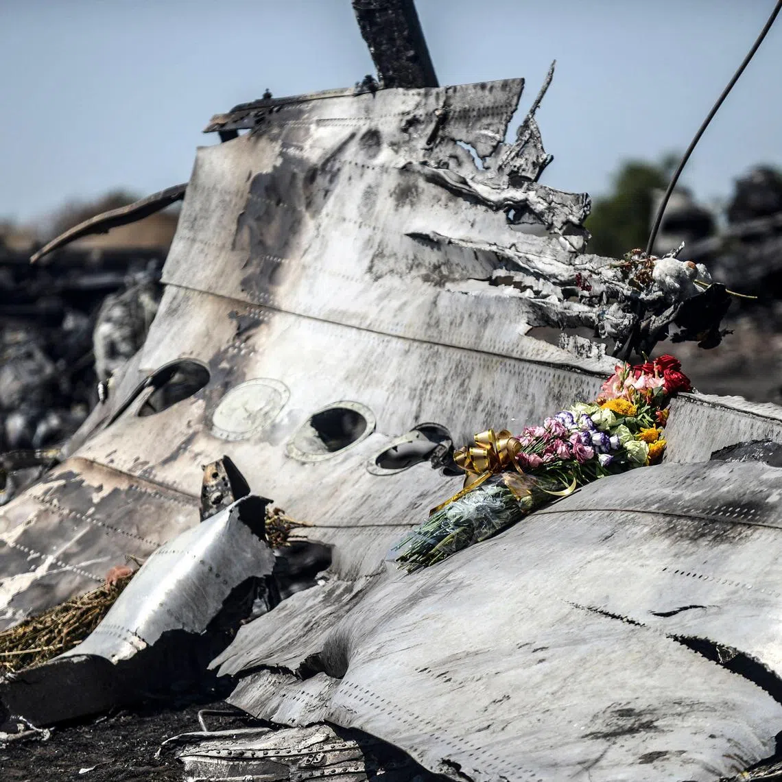 (FILES) This photograph shows flowers, left by parents of an Australian victim of the crash on a piece of the Malaysia Airlines flight MH17, near the village of Hrabove (Grabove), in the Donetsk region on July 26, 2014. The families of the victims of the downing of flight MH17 in war-torn eastern Ukraine are this week commemorating ten years since the tragedy, with dwindling hopes of seeing those responsible behind bars. (Photo by Bulent KILIC / AFP)