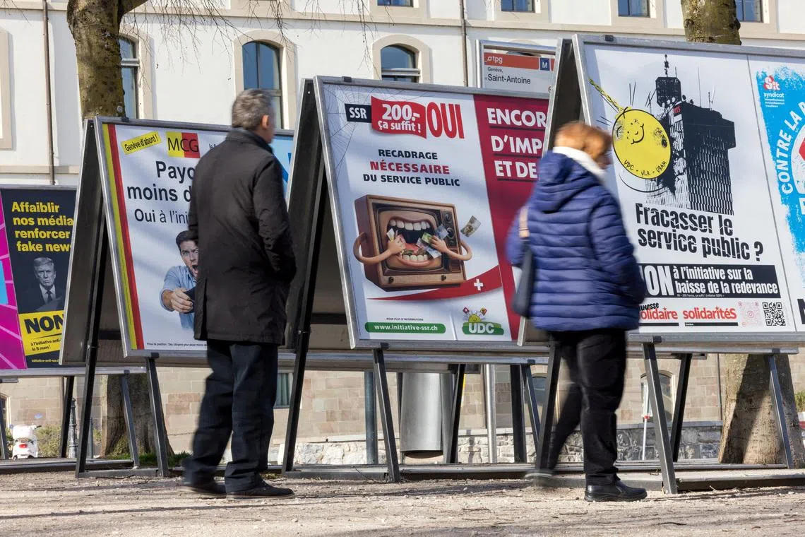 FILE PHOTO: People stand next to posters about funding cuts to the SRG SSR (Swiss Broadcasting Corporation), ahead of the upcoming Swiss national referendum on March 8, in Geneva, Switzerland, February 15, 2026. REUTERS/Pierre Albouy/File Photo