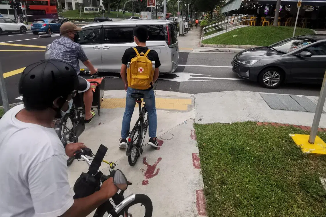 Three cyclists stopping for cars. Such pro-car road design causes more stops for those riding on cycling paths and pavements.