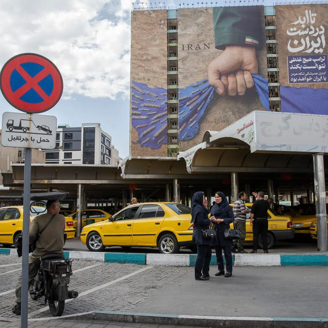 People pass near a billboard depicting a hand representing Iran holding the Strait of Hormuz, in Tehran, Iran, on April 21.