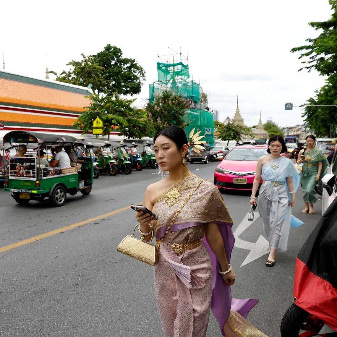 Foreign tourists wearing Thai traditional costumes walk at a tourist spot outside Wat Pho Temple, or the Temple of the Reclining Buddha in Bangkok.