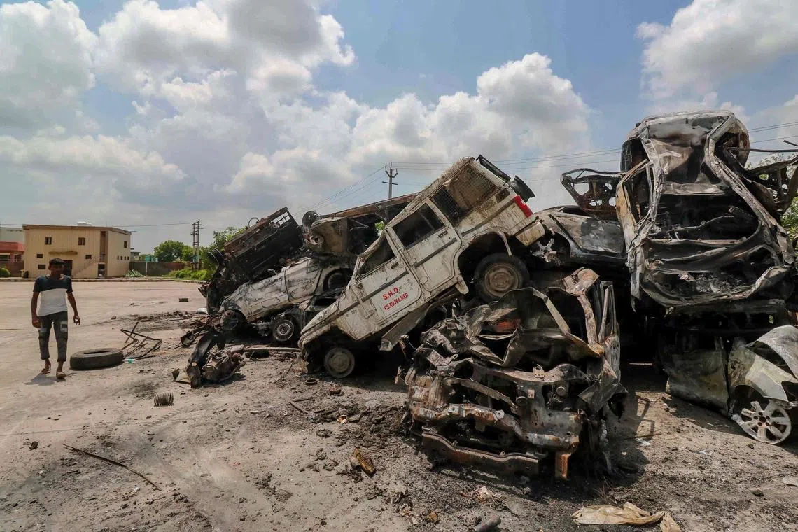A man walks past burned vehicles after violent communal clashes in Nuh, near the Indian capital New Delhi.