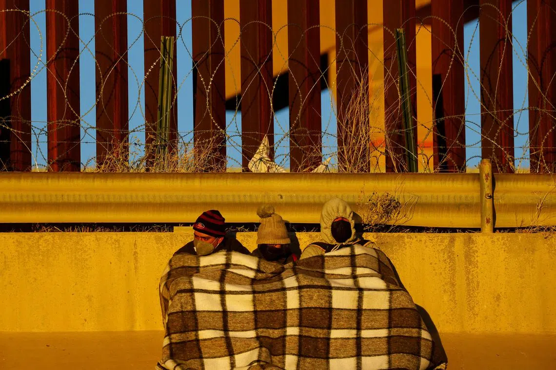 Migrants sit near the border wall after crossing the Rio Bravo river to turn themselves in to U.S. Border Patrol agents to request asylum in the U.S. city of El Paso, Texas, as seen from Ciudad Juarez, Mexico December 14, 2022. 