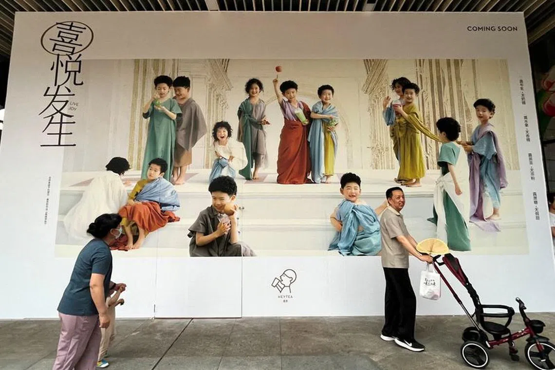 A man pushes a stroller and a woman holds a child as they walk past a billboard in Shenzhen, Guangdong province, China April 21, 2023. REUTERS/David Kirton/File Photo
