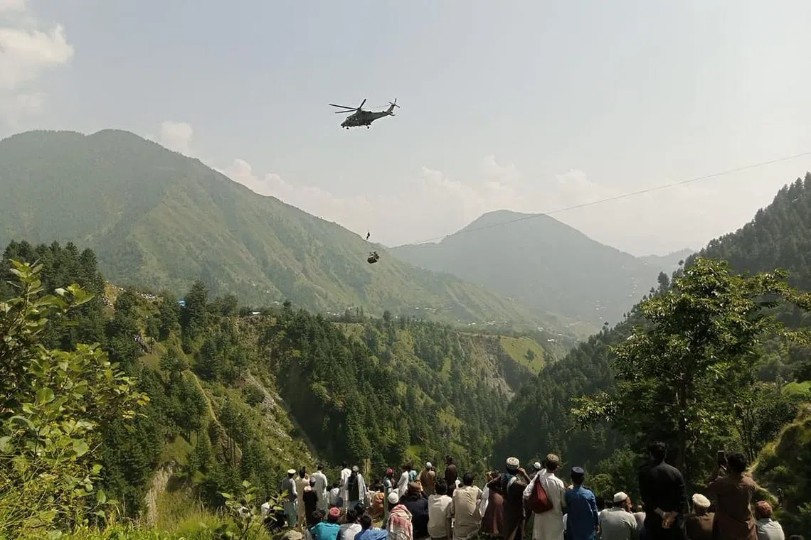 People watch as an army soldier slings down from a helicopter during the rescue mission to recover students stuck in a cable car.