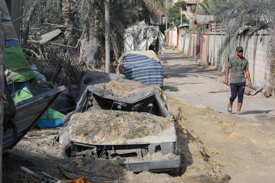 A man walks past a wrecked car at the site of Israeli bombardment in Khan Yunis city in the southern Gaza Strip on July 14, 2024.