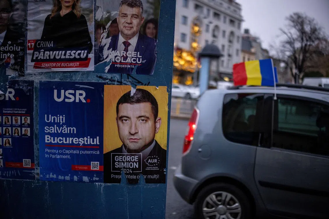A car with a Romanian flag drives past posters depicting Prime Minister Marcel Ciolacu and Leader of the radical right Alliance for Uniting Romanians (AUR) George Simion, a day before the parliamentary election, in Bucharest, Romania, November 30, 2024. REUTERS/Alkis Konstantinidis