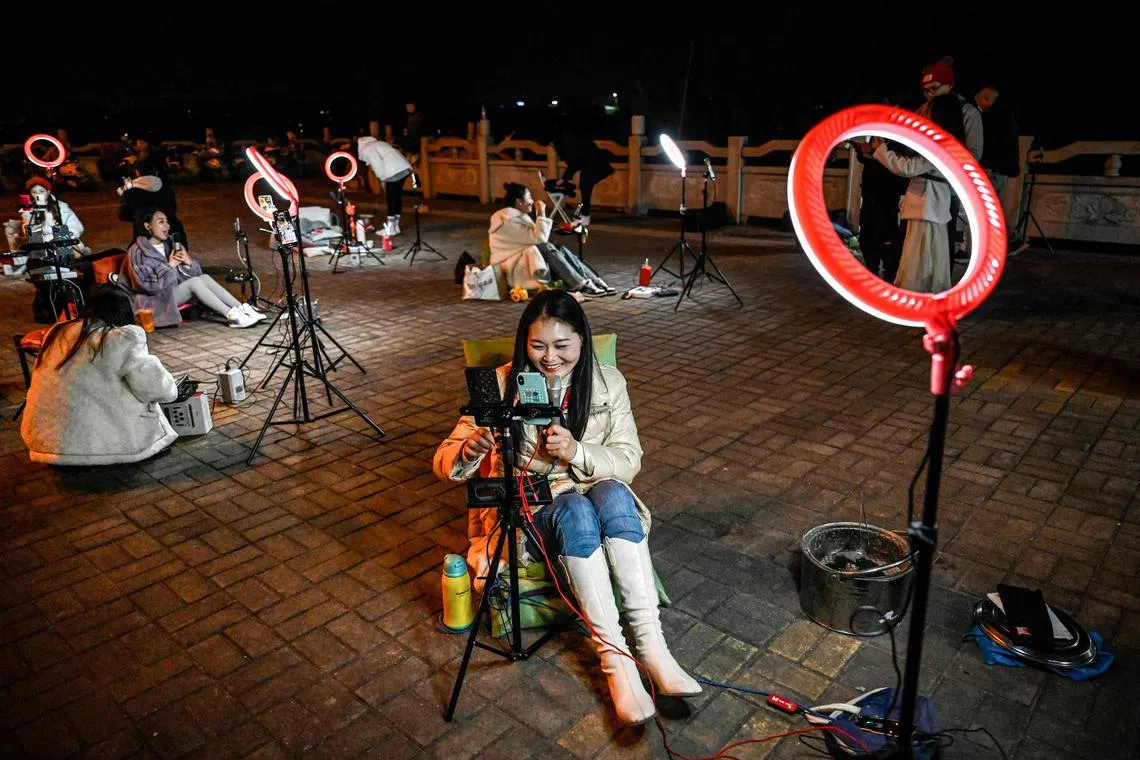 The photo taken on February 20, 2023 shows outdoor livestreamers singing and chatting with the audiences through their mobile phones on an overpass bridge at night in Guilin, in southern China's Guangxi province. - In the dead of night on a bridge in southern China, around two dozen livestreamers sat crooning and chatting into microphones, their identical ring lights spaced a few metres apart in glowing rows. (Photo by Jade GAO / AFP) / To go with "China-tech-lifestyle-offbeat", SCENE by Vivian LIN