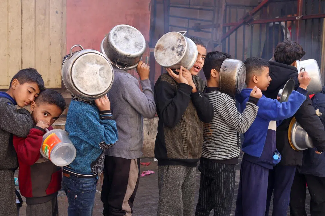 Palestinian children carry pots as they queue to receive food cooked by a charity kitchen, amid shortages in food supplies, as the conflict between Israel and Hamas continues, in Rafah in the southern Gaza Strip December 14, 2023. REUTERS/Saleh Salem/File Photo