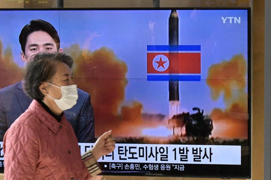 TOPSHOT - A woman walks past a television showing a news broadcast with a file photo of a North Korean missile test, at a railway station in Seoul on November 17, 2022. (Photo by Anthony WALLACE / AFP)