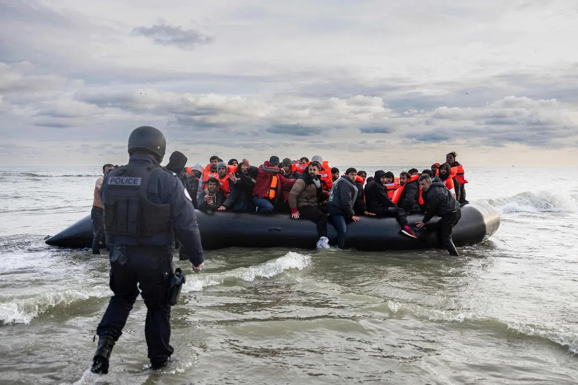 A French police officer prepares to puncture a smuggler's boat with a knife to prevent migrants from trying to cross the English Channel to Britain.