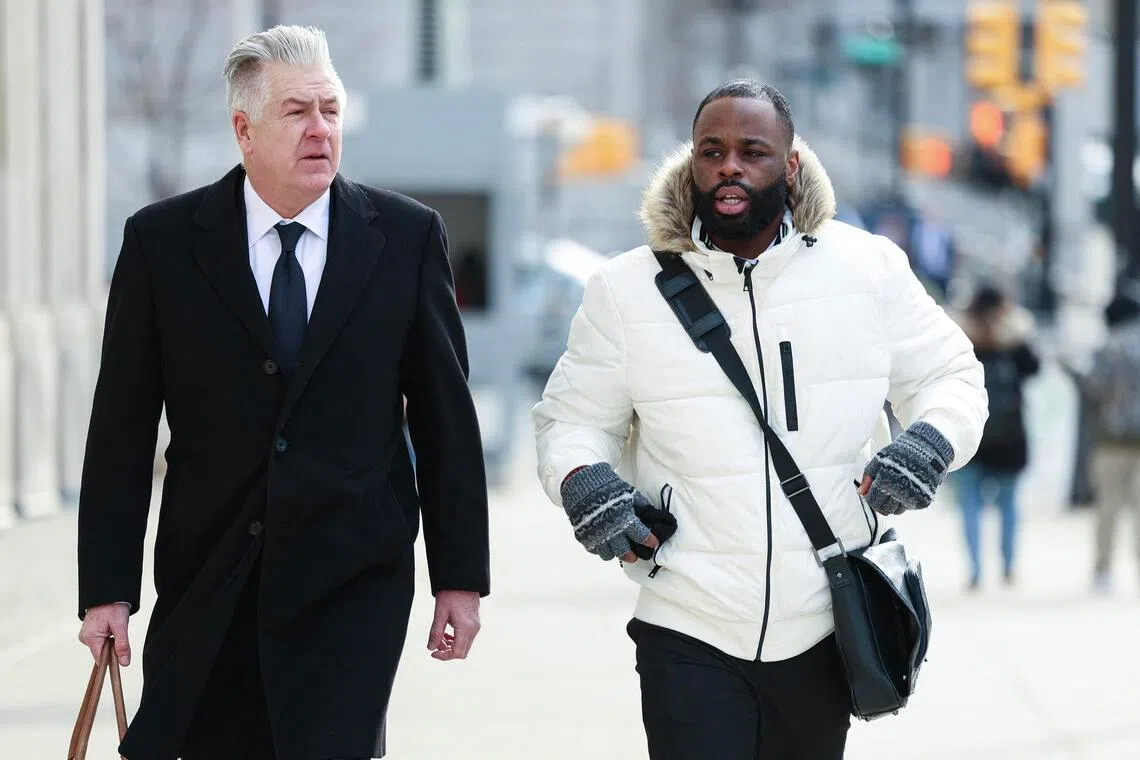 Two men walking on a city sidewalk, one in a suit and one in a white jacket.