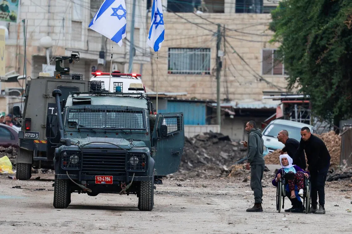A man pushes a Palestinian woman in a wheelchair, as Palestinians leave Jenin camp during an Israeli raid, in the Israeli-occupied West Bank on Jan 22.