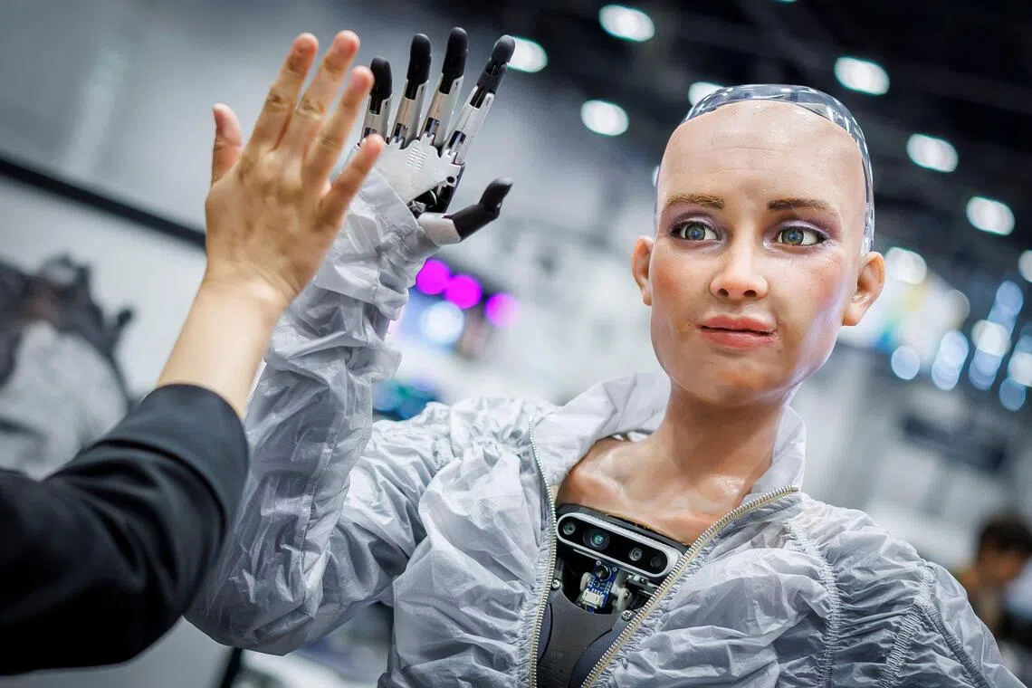 Sophie, a robot using artificial intelligence from Hanson Robotics, shares a high five with a visitor during the International Telecommunication Union (ITU) AI for Good Global Summit in Geneva on July 8, 2025. (Photo by Valentin Flauraud / AFP)
