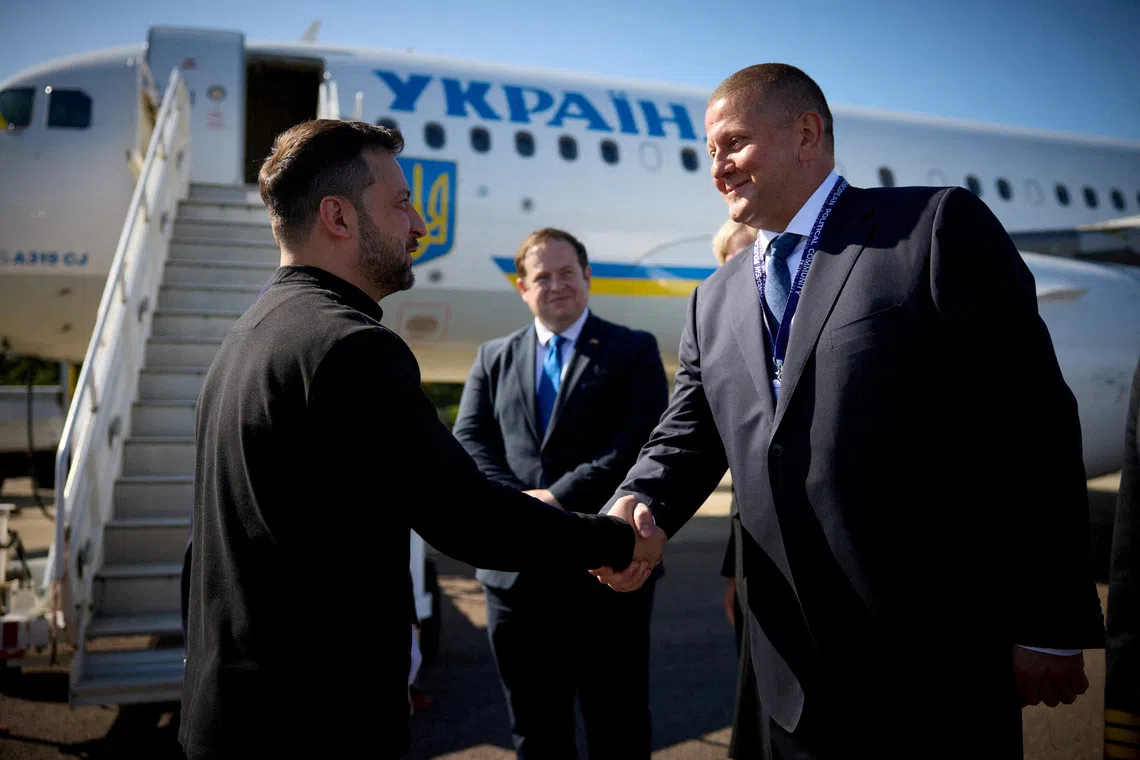 Two men shaking hands in front of a Ukrainian airplane.