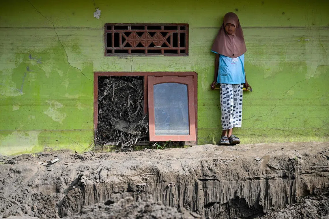 A child stands on hardened mud beside the window of a residence damaged by flash floods in Aceh, after devastating floods and landslides struck Sumatra late in 2025.