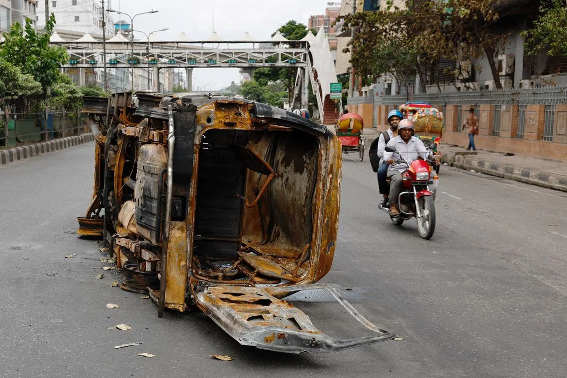Men ride on a motorbike past a damaged vehicle that was set afire by a mob during clashes after violence erupted following protests by students against government job quotas, in Dhaka, Bangladesh, July 22, 2024. REUTERS/Mohammad Ponir Hossain/ File Photo