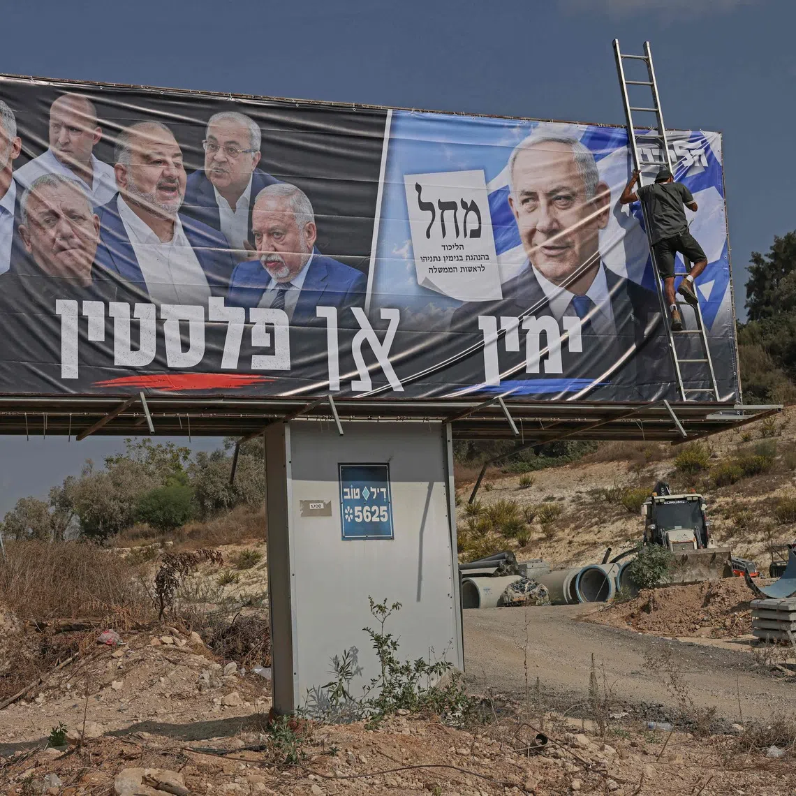 A worker unfurls an electoral campaign billboard for Israel’s Prime Minister Benjamin Netanyahu’s Likud party, alongside the faces of the members of the opposition.