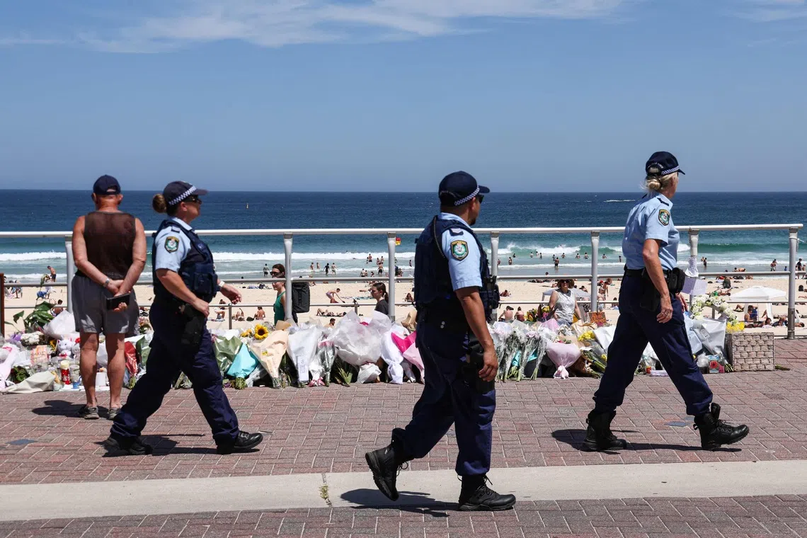 Police officers walking past floral tributes left at the promenade of Bondi Beach in Sydney on Dec 18.