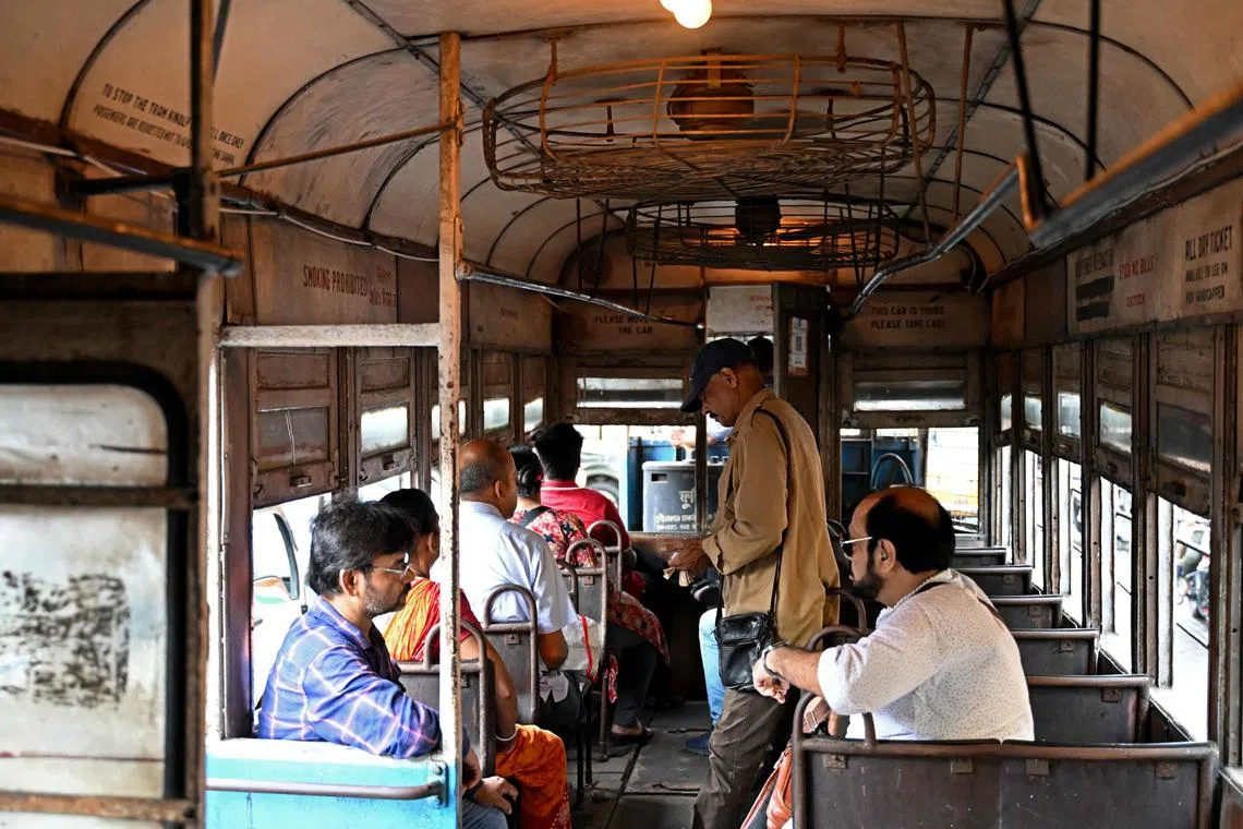 In this photo taken on September 8, 2024, a conductor (2R) collects tickets as passengers commute in a tram along a street in Kolkata. Introduced in the sprawling eastern city in 1873 during the early days of the imperial British Raj, trams in Kolkata were initially horse-drawn, then steam-driven. Electric-powered trams took to the streets in 1900. The single-storey trams -- painted in uniform stripes of bright blue and white, with a sunshine yellow top -- trundle at best at around 20 kilometres (12 miles) per hour, if not snarled in traffic blocking its route. (Photo by Dibyangshu SARKAR / AFP) / To go with “Asia’s oldest operating trams see slow death in India” FOCUS