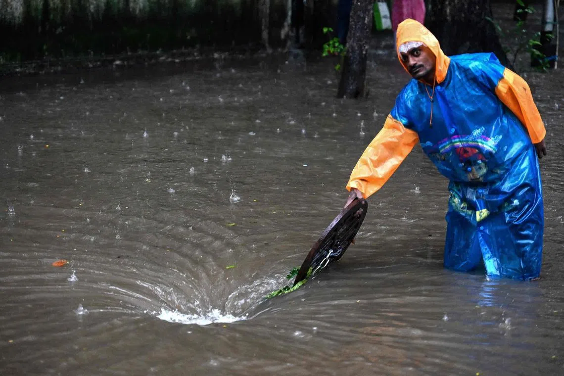 TOPSHOT - A municipal worker stands to guide vehicles away from a manhole along a flooded street during rainfall in Mumbai, on July 21, 2024. (Photo by Sujit JAISWAL / AFP)