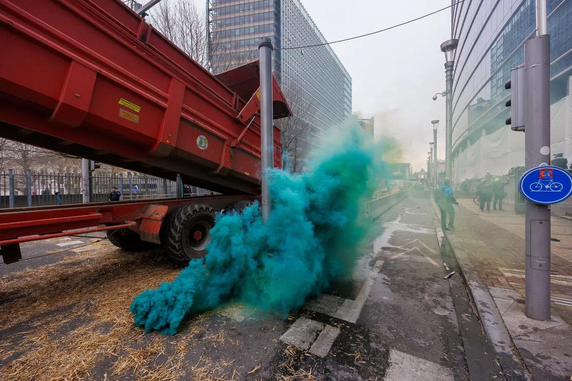 Farmers drop earth between flares lit by protesters on the side of an Agriculture and Fisheries Council in Brussels.
